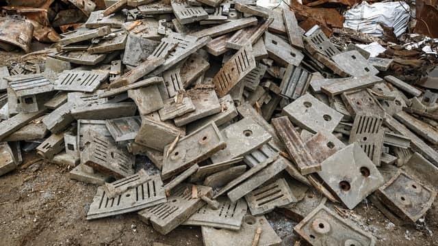 Cast metal machine parts and plates piled on a scrapyard floor.