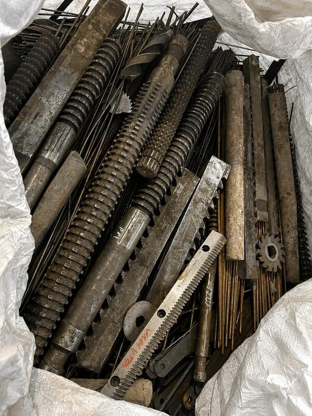 Machined steel shafts, screws and gears collected in a bulk bag.