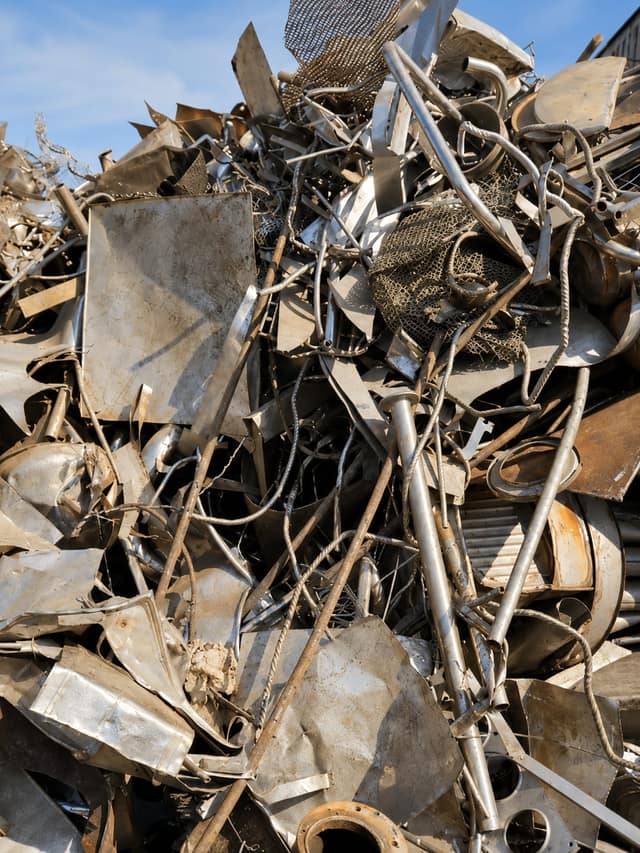 A mixed metal scrap pile of sheet offcuts, wire and cable under open sky.